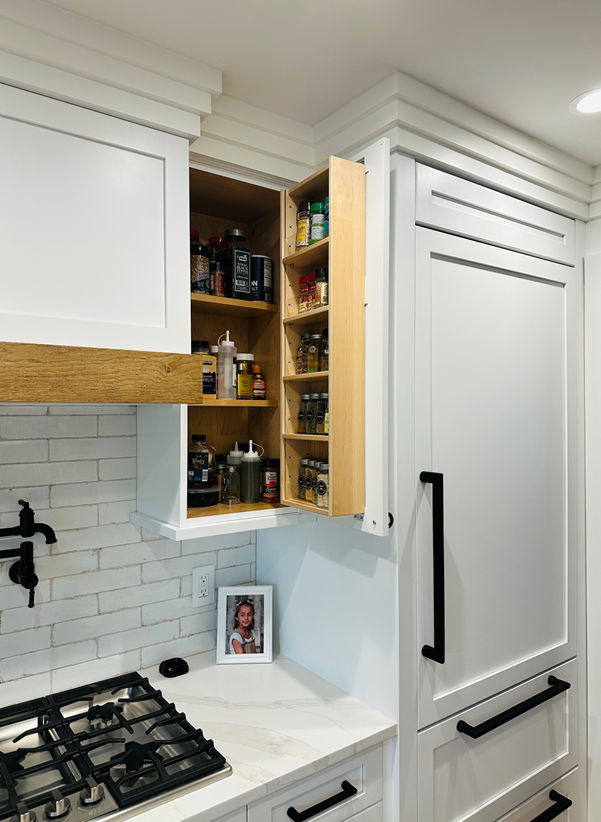 White kitchen corner with open spice cabinet and gas stove beside a tall pantry cabinet