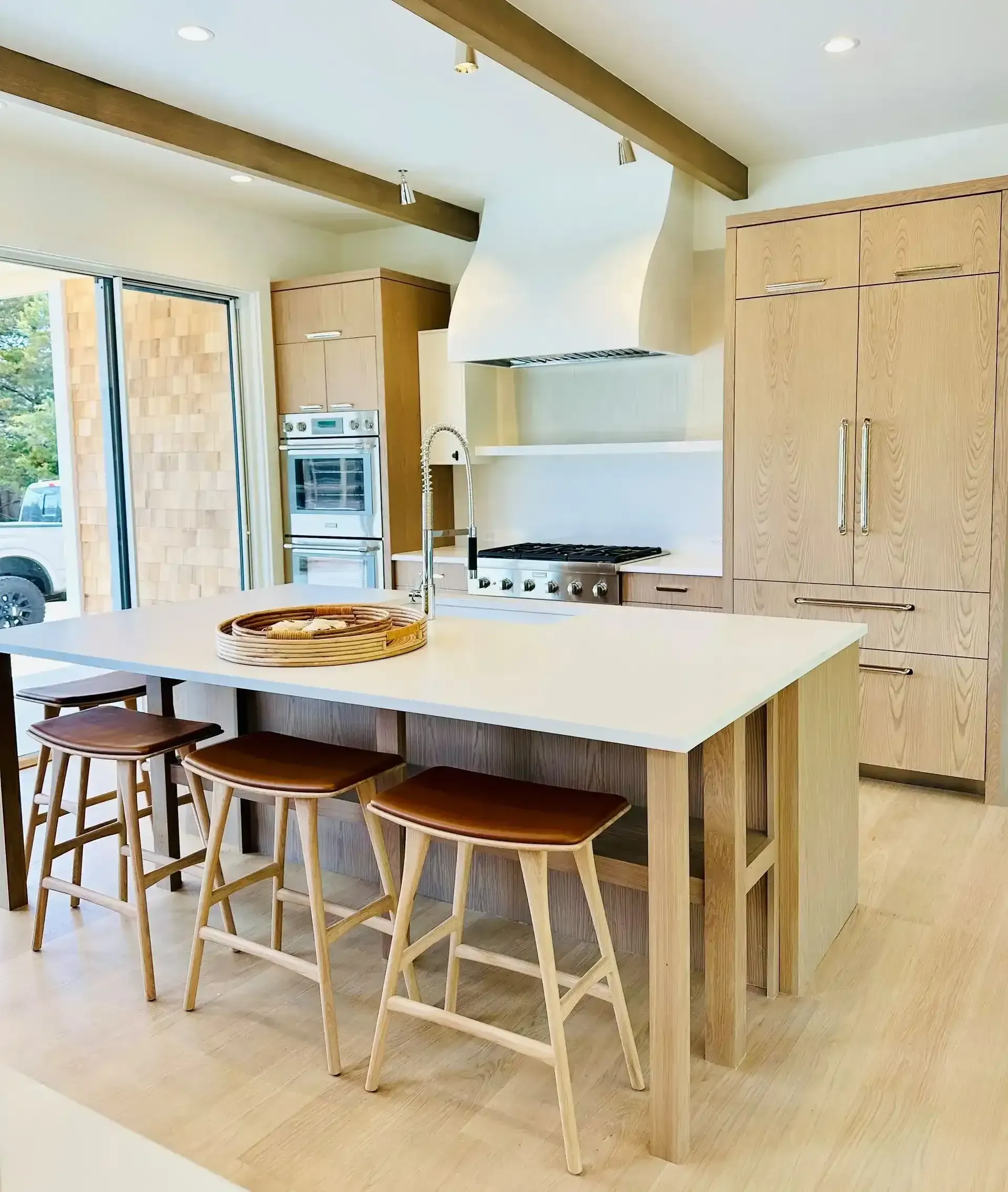 Modern wood kitchen with built-in oven, countertop appliances, and light marble backsplash.