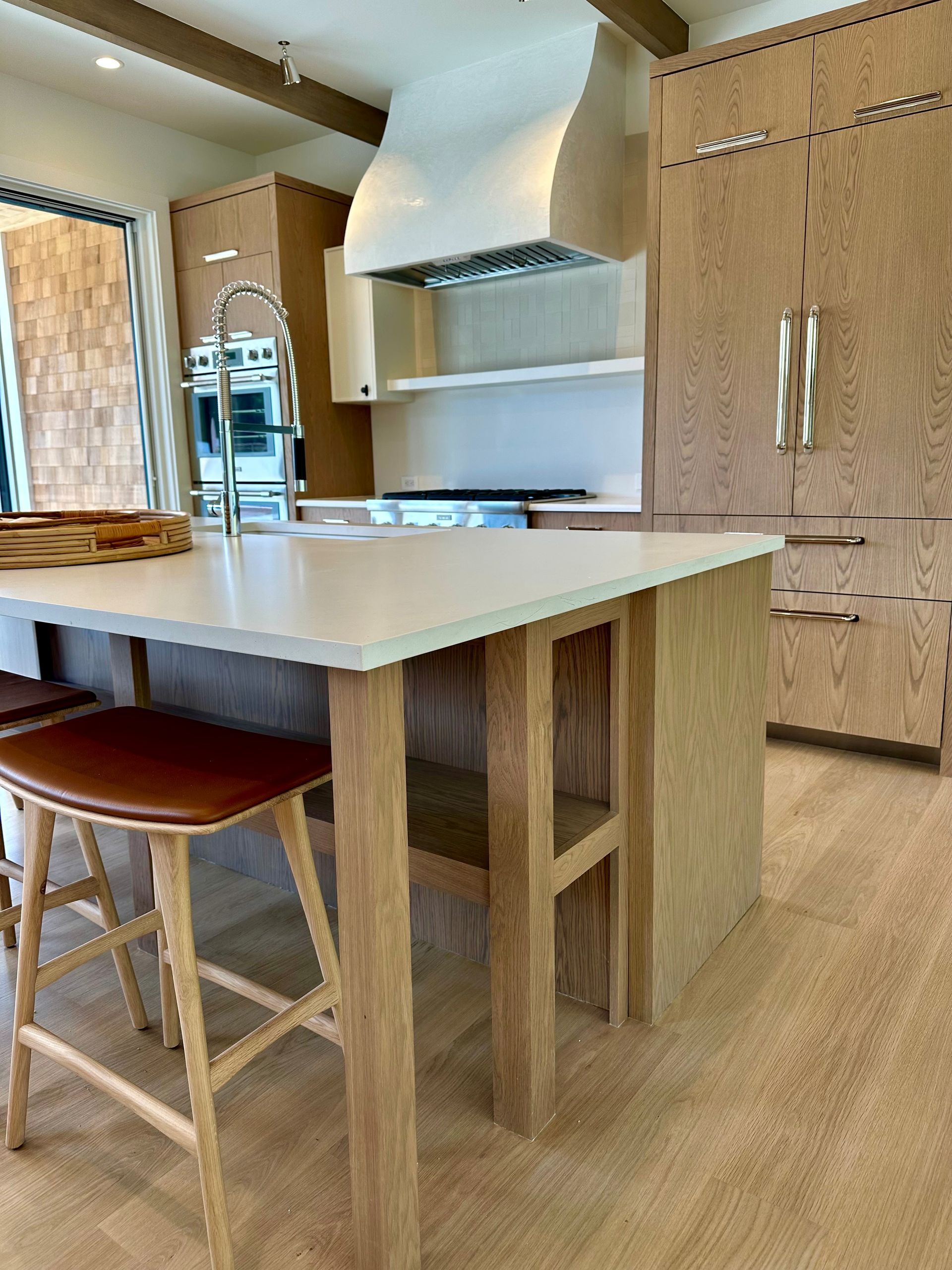 Modern kitchen with white island, bar stools, wood cabinets, and stainless steel range hood