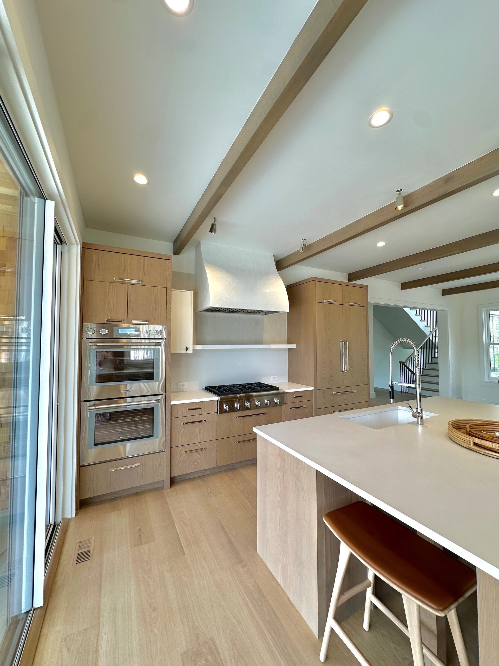 Bright modern kitchen with wood cabinets, white island, stainless appliances, and vaulted ceiling beams