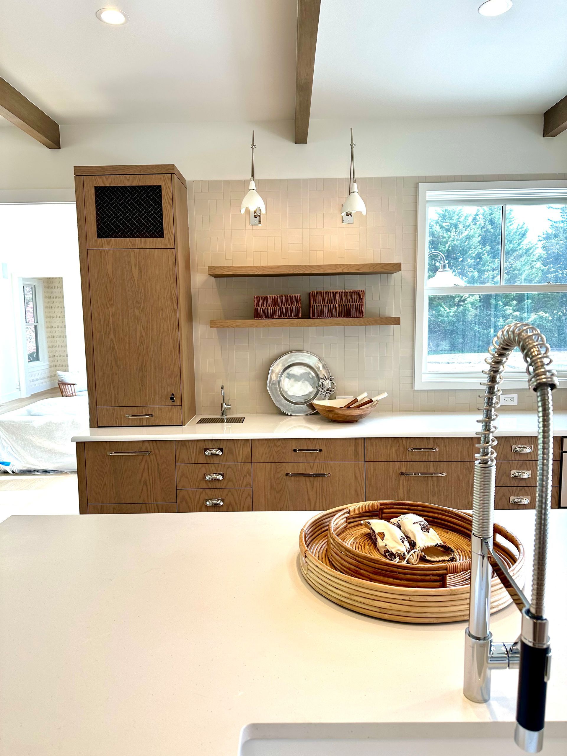 Bright kitchen with white island, wood cabinets, pendant lights, and a large window above the sink.