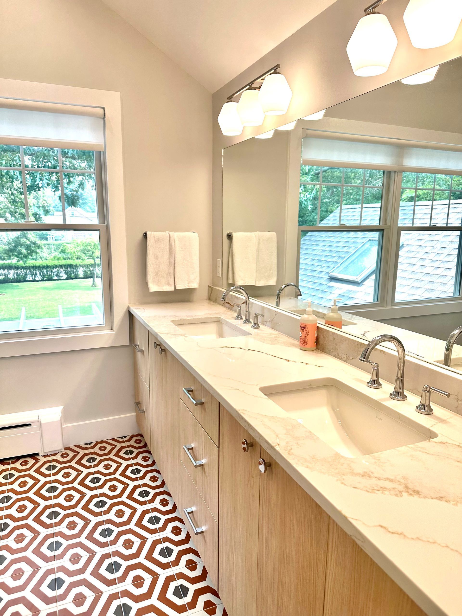 Bright bathroom with double vanity, large mirror, white countertop, and patterned tile floor.