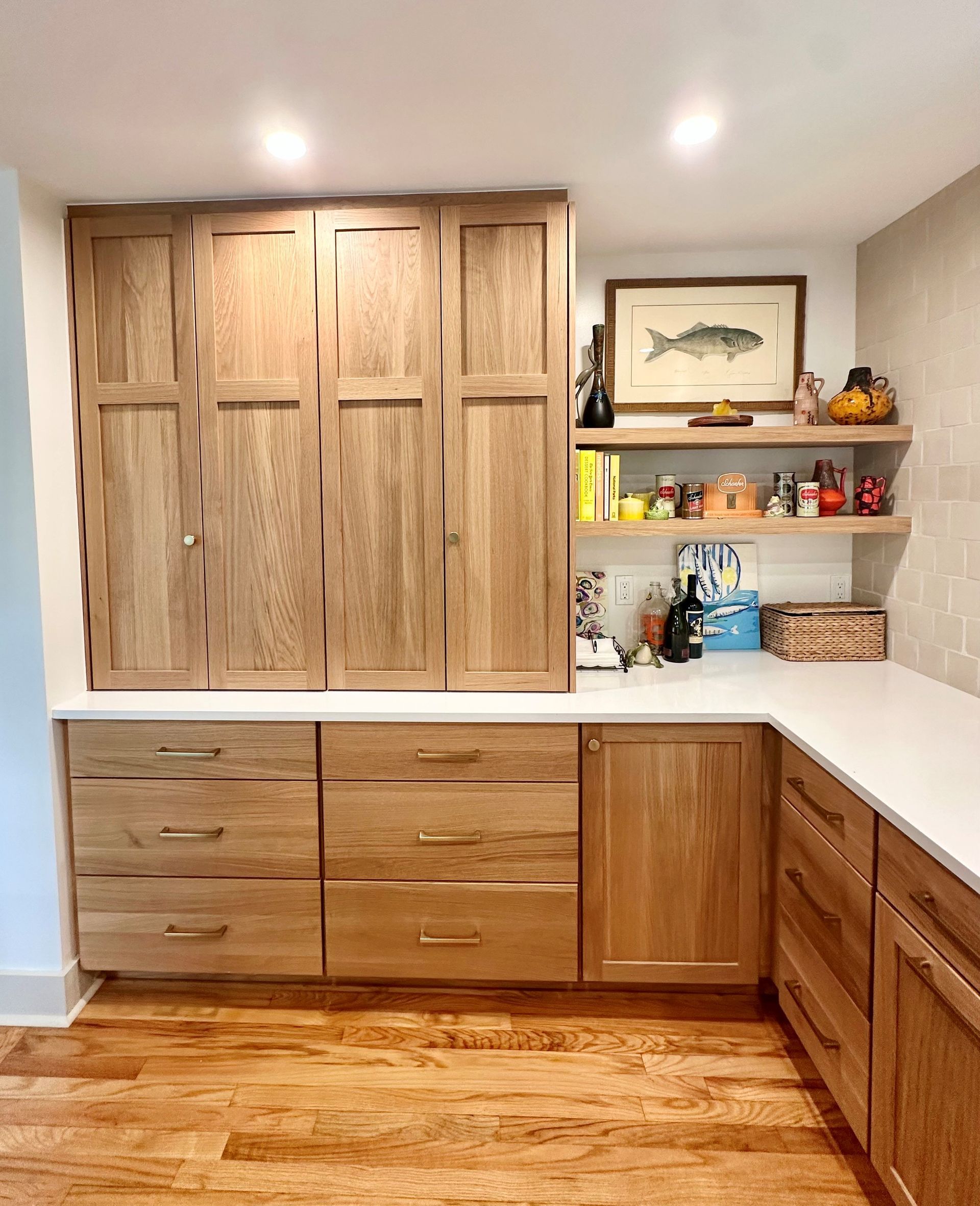 Built-in wood cabinets and white countertops in a kitchen nook with open shelves and a brick backsplash.