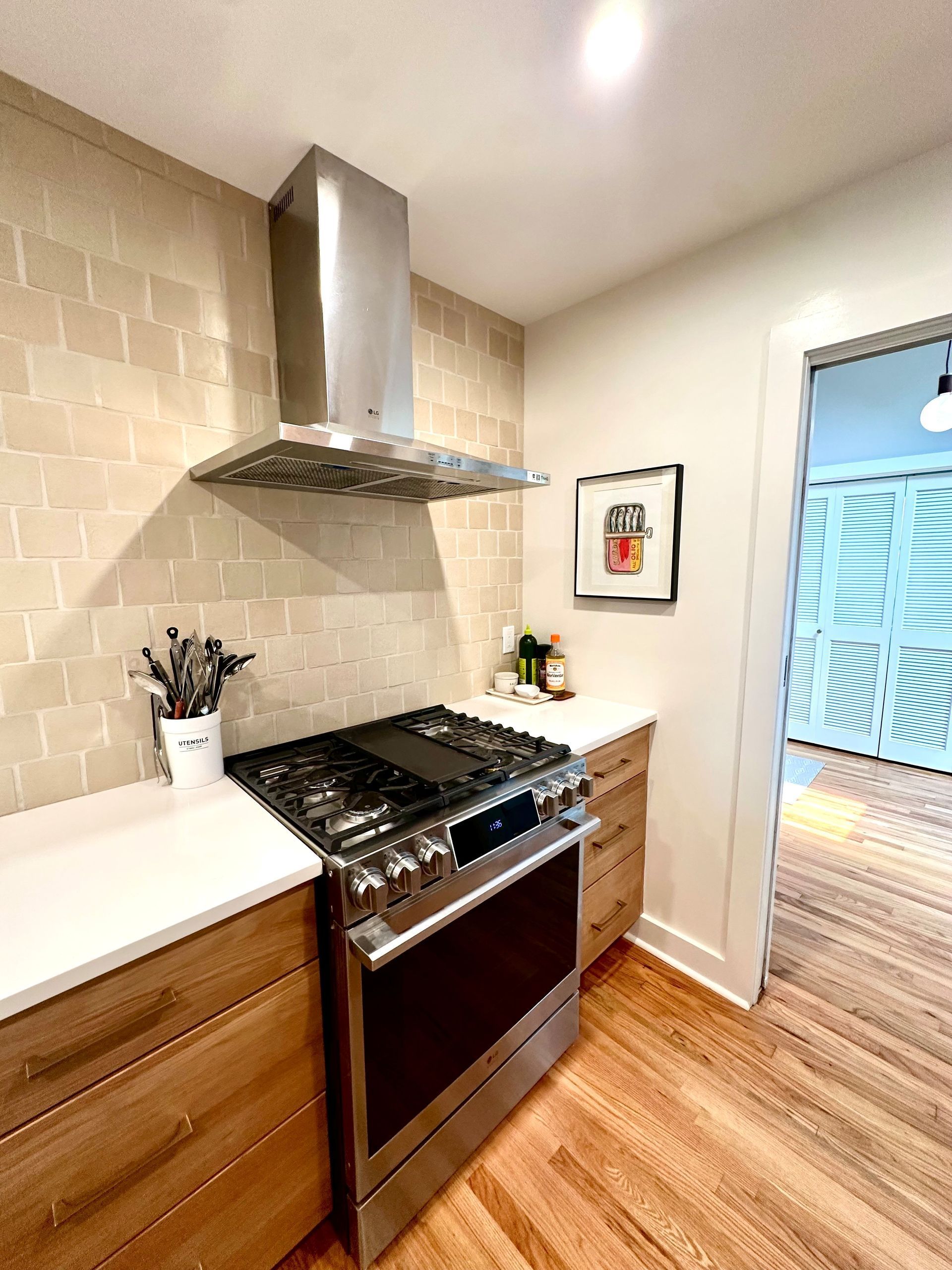 Small modern kitchen with stainless steel stove, range hood, wood floor, and glass door to patio.