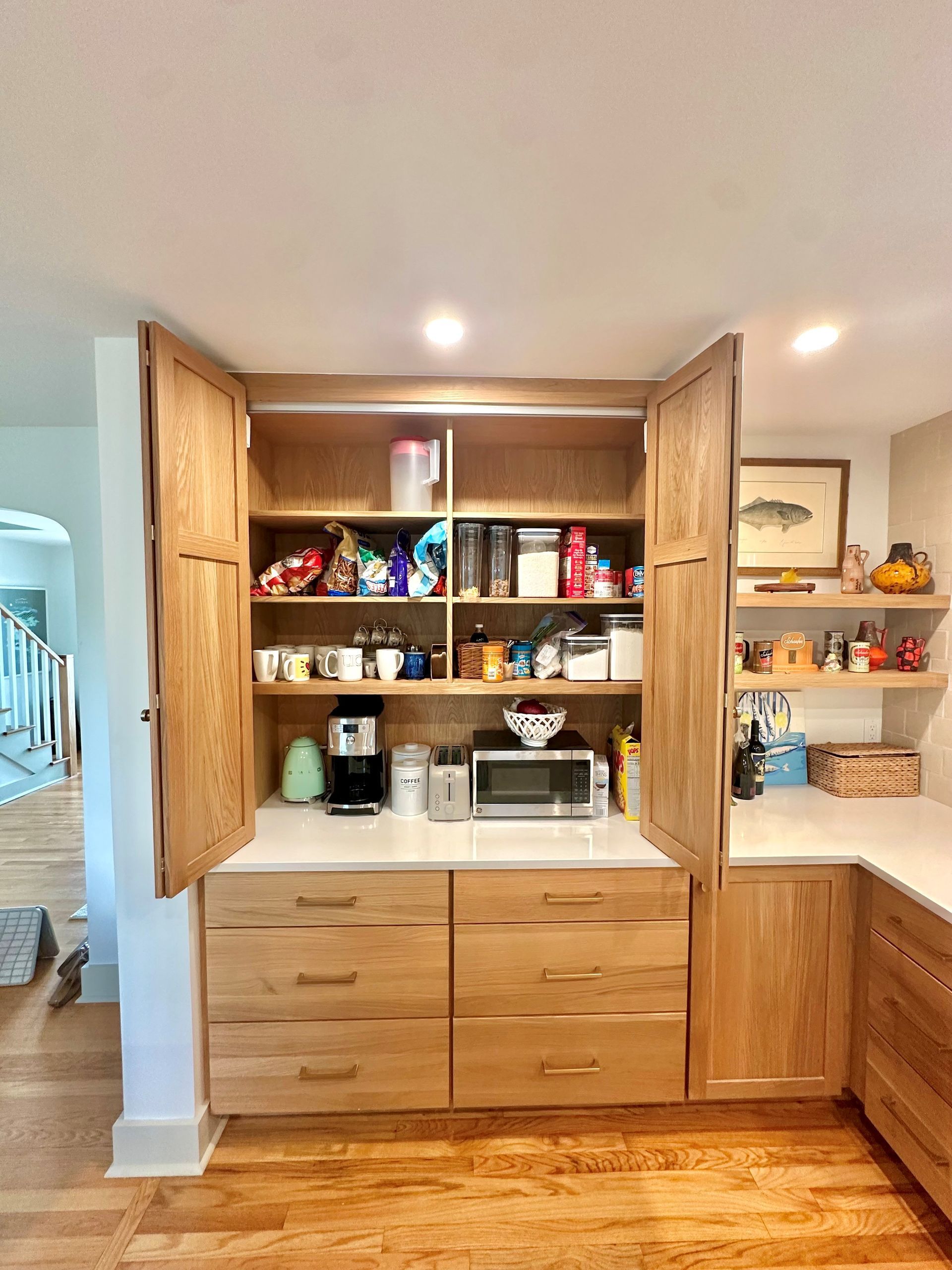 Built-in kitchen pantry with open wooden cabinets and shelves stocked with snacks, dishes, and appliances.