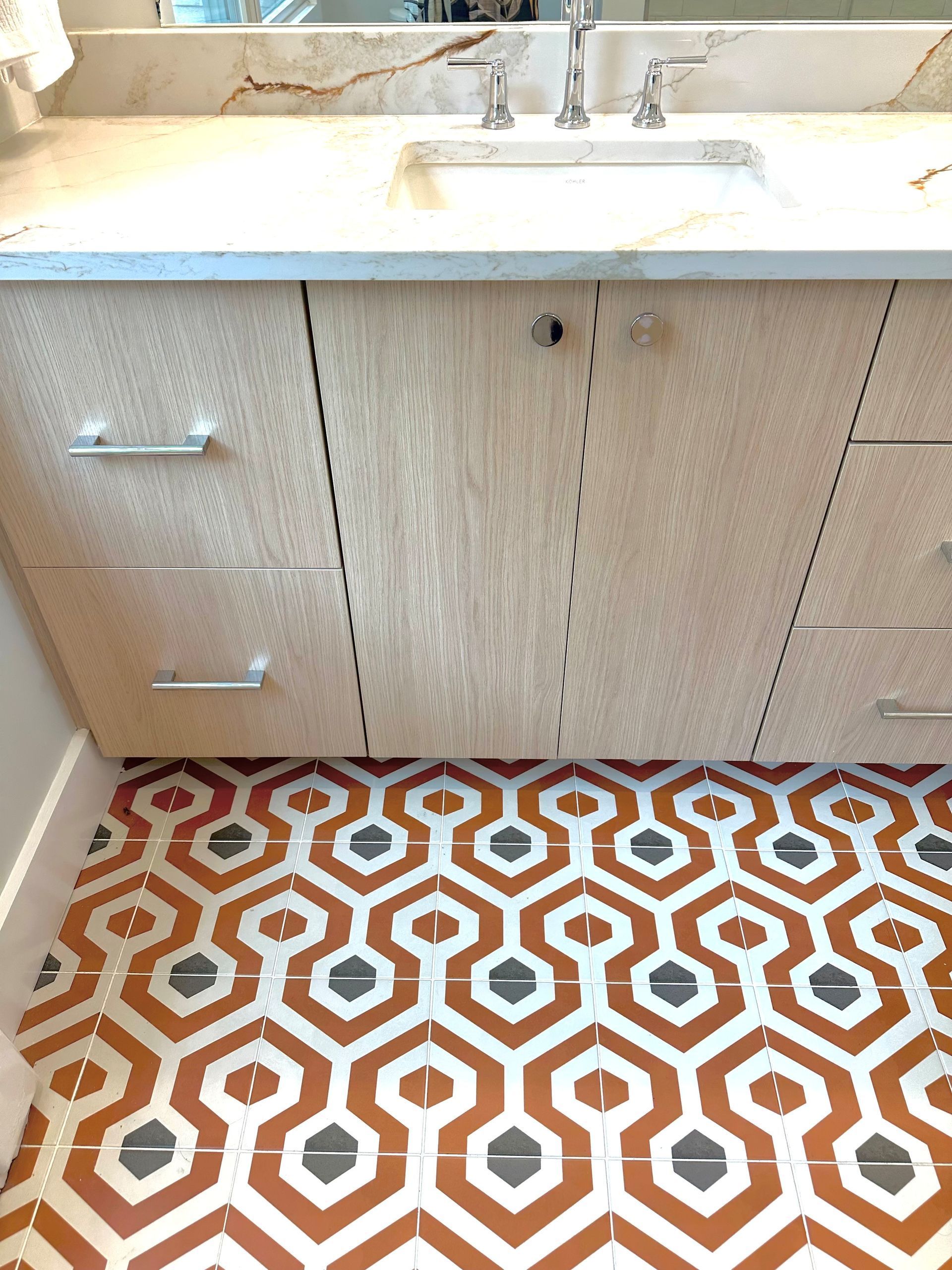 Bathroom vanity with white countertop, beige cabinet, and orange patterned tile floor