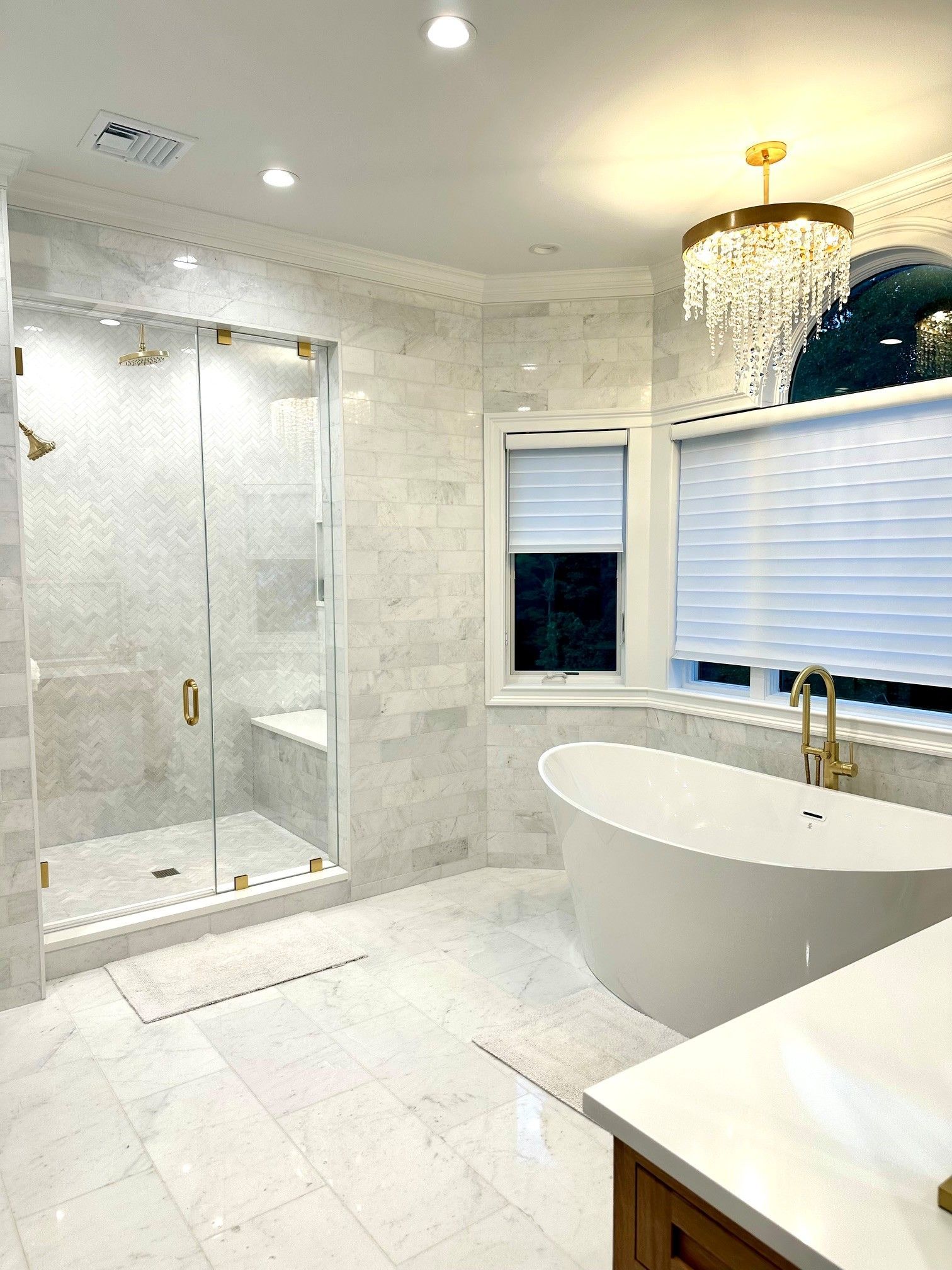 Bright white luxury bathroom with glass shower, freestanding tub, and gold fixtures
