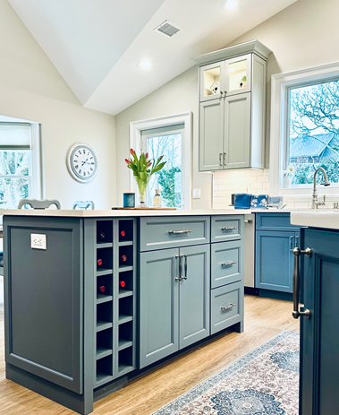 Bright kitchen with gray island, white cabinets, and blue accents, shown in a sunlit room.