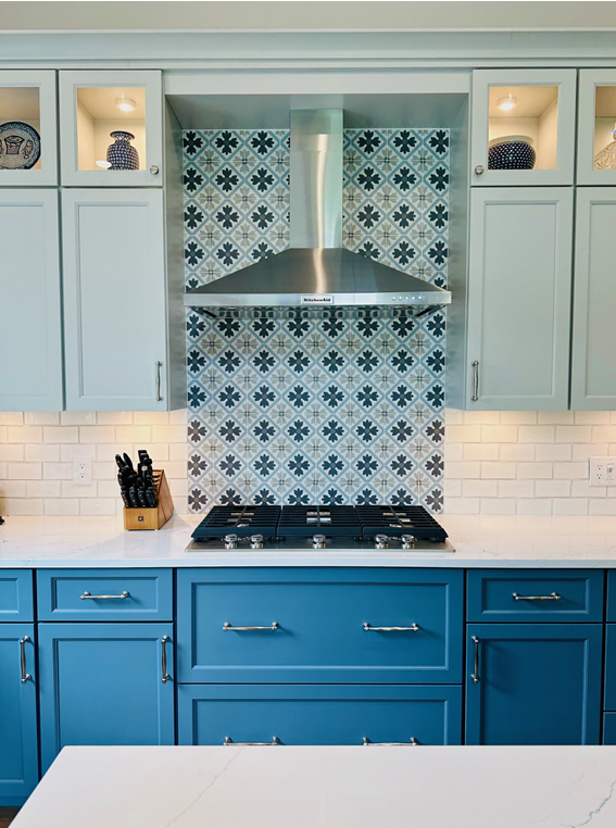 Blue-and-white kitchen with patterned tile backsplash, stainless range hood, and teal cabinets
