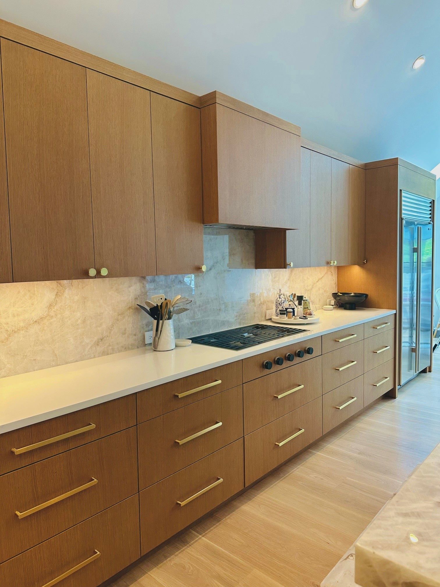 Modern kitchen with wood cabinets, white countertops, and stainless appliances along a bright wall.