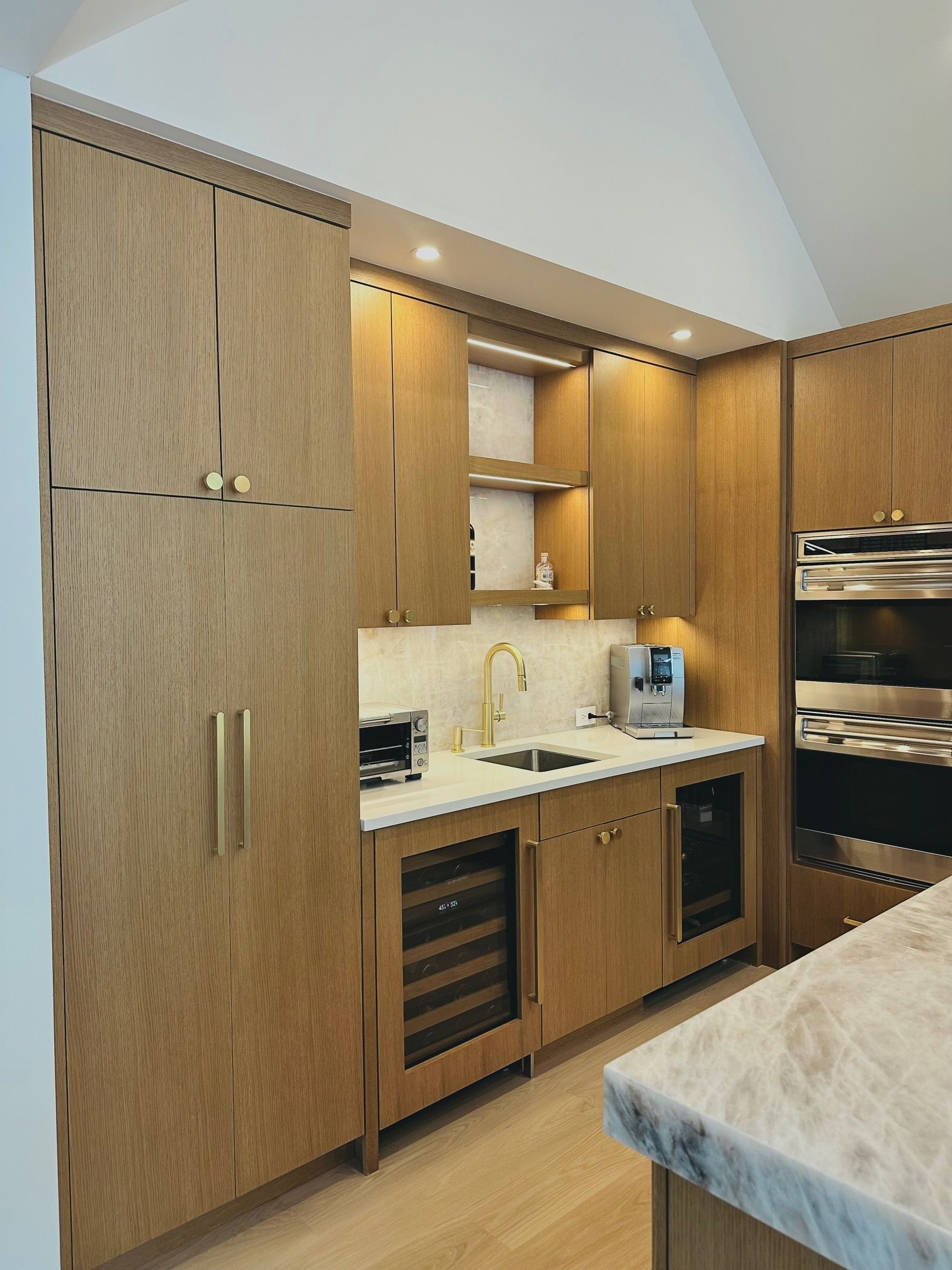Modern kitchen with wood cabinets, built-in ovens, and a marble island counter
