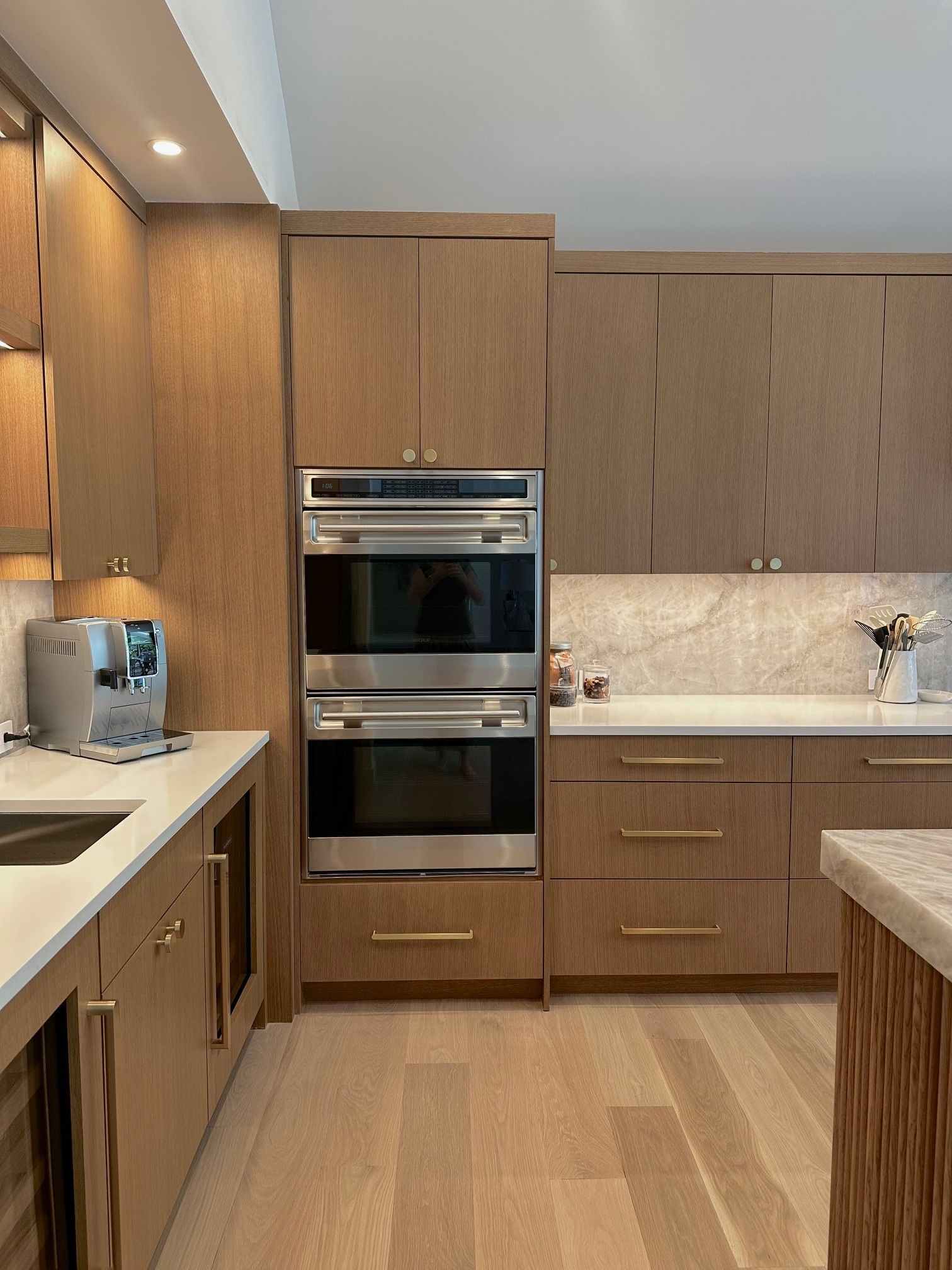Modern kitchen with wood cabinets, built-in ovens, light countertops, and a wood floor.