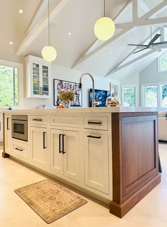 Bright modern kitchen island with white cabinets, wood trim, pendant lights, and a sink under vaulted ceilings
