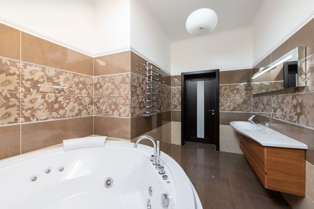 Modern bathroom with a corner whirlpool tub, sink vanity, brown tile walls, and dark door.
