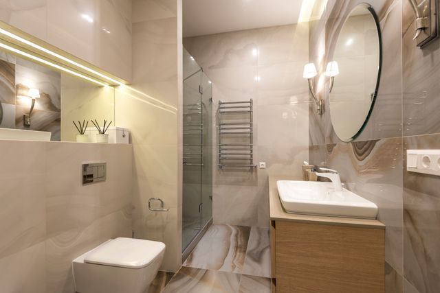 Modern beige bathroom with glass shower, sink, toilet, and round mirror