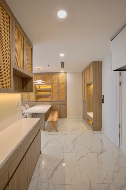 Modern kitchen with wood cabinets, marble floor, and a built-in desk area under warm ceiling lights