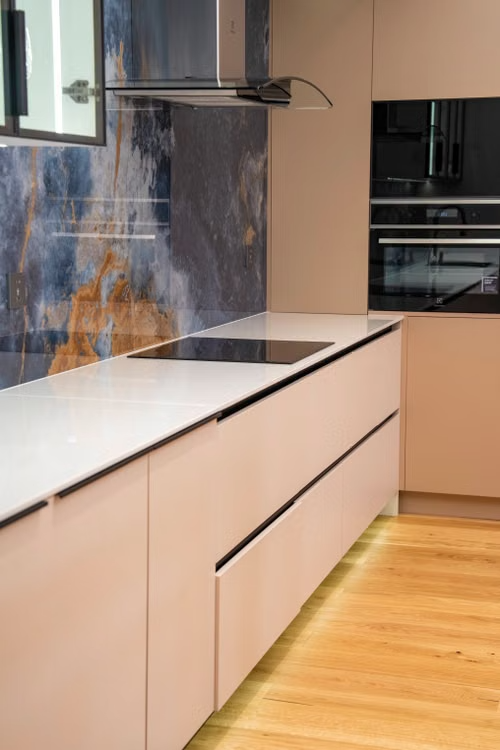 Modern kitchen with pale cabinets, white countertop, black cooktop, and wood flooring