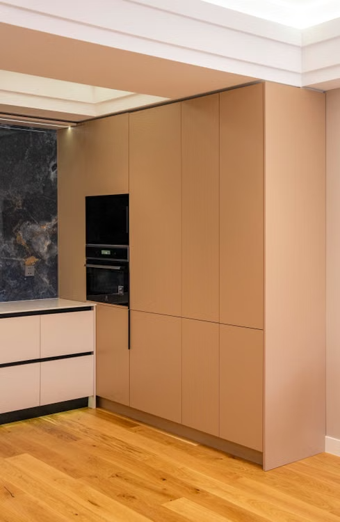 Built-in tan cabinets and black oven in a modern kitchen with light wood floor