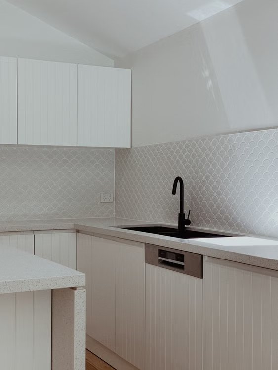 Modern white kitchen with cabinets, black faucet, and light patterned backsplash