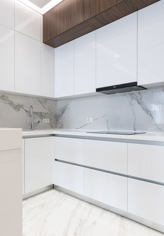 Modern white kitchen with glossy cabinets, marble backsplash, and wood ceiling trim