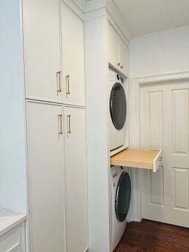 Compact laundry room with beige tile walls, sink counter, and a front-loading washer
