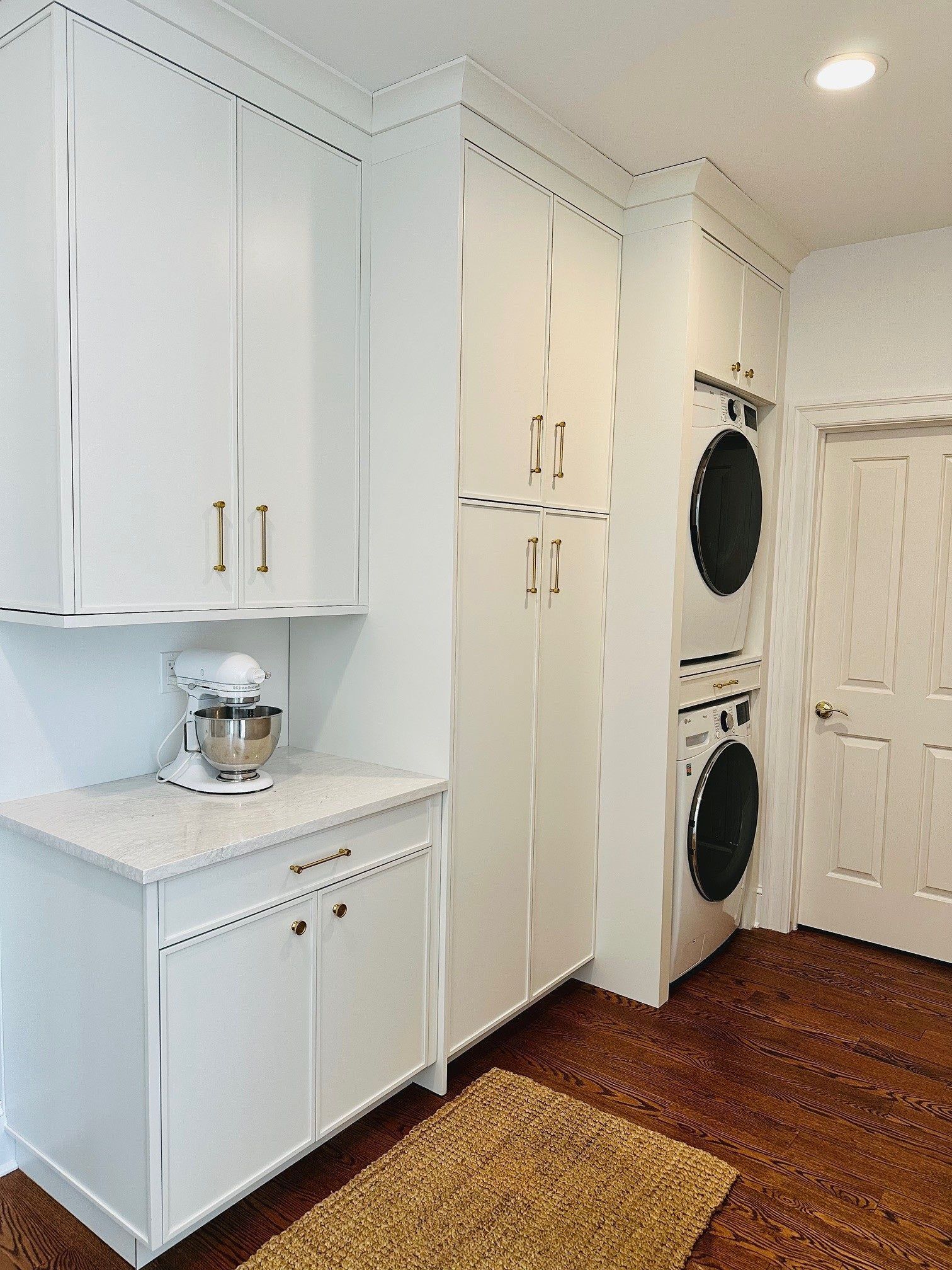 White laundry room with cabinets, countertop mixer, stacked washer and dryer, and wood floor.