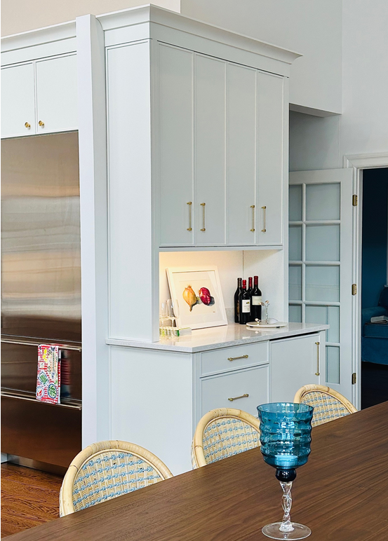 Bright kitchen with white cabinets, stainless fridge, and a wooden dining table with blue glassware
