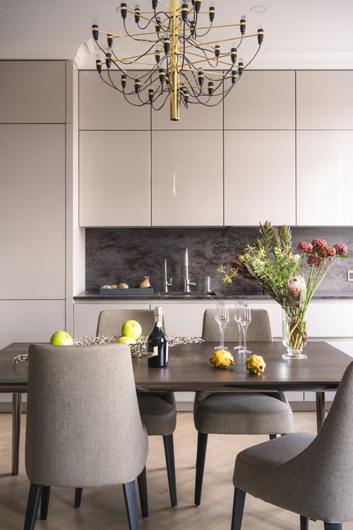Modern dining room with gray chairs, dark table, white cabinets, and a chandelier under soft light