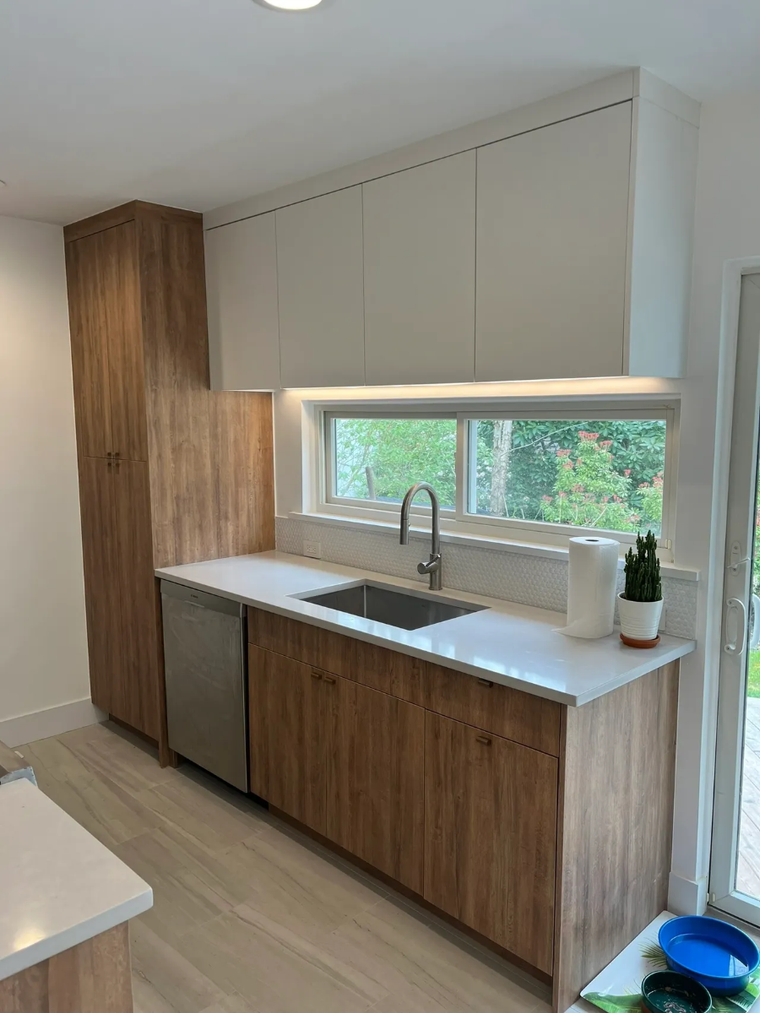 Modern kitchen with wood cabinets, white countertops, sink, and a large window over the counter