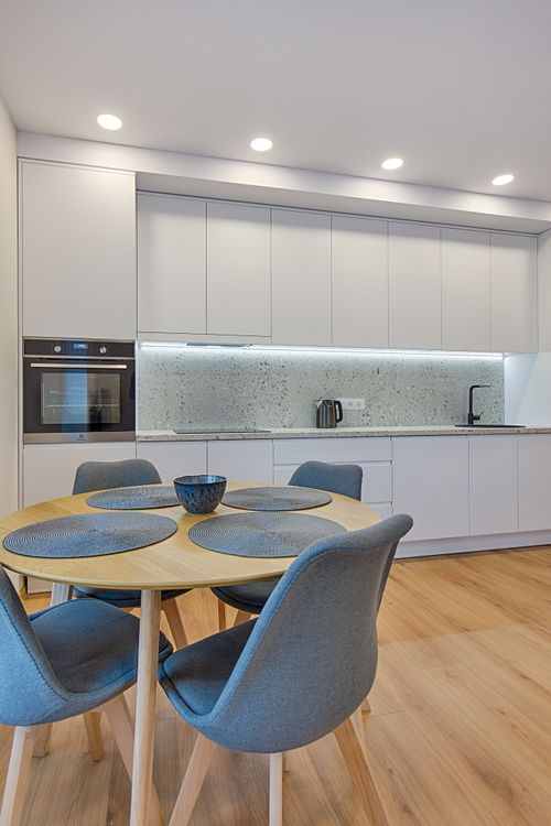 Modern white kitchen with round dining table, blue chairs, and under-cabinet lighting