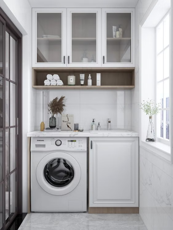 Compact white laundry nook with washer, sink, shelves, and cabinets beside a window