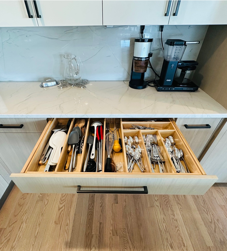 Kitchen drawer with neatly organized silverware and cooking utensils under a white countertop and cabinets