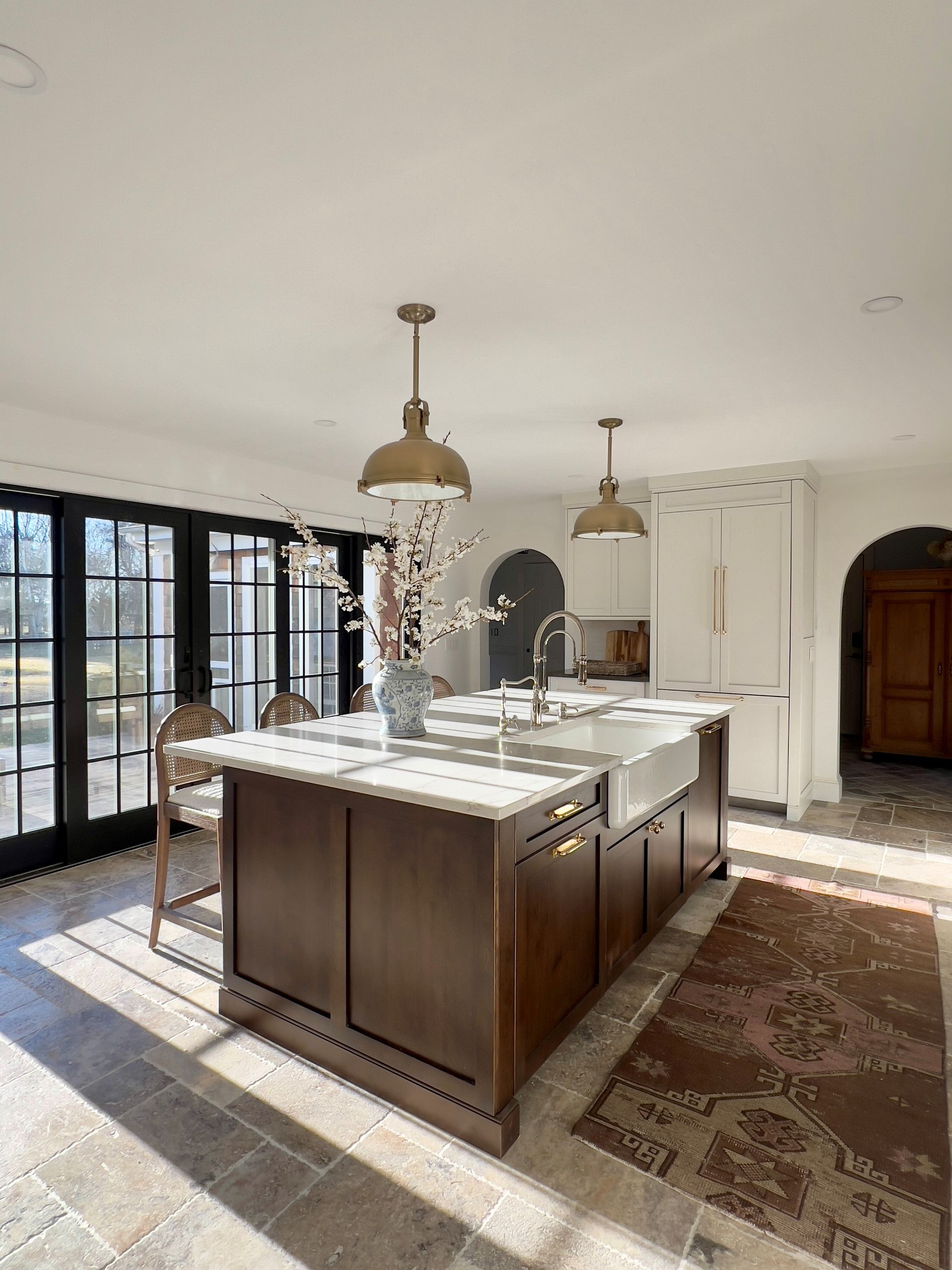 Bright kitchen with a large island, pendant lights, black-framed windows, and a patterned rug on the floor.