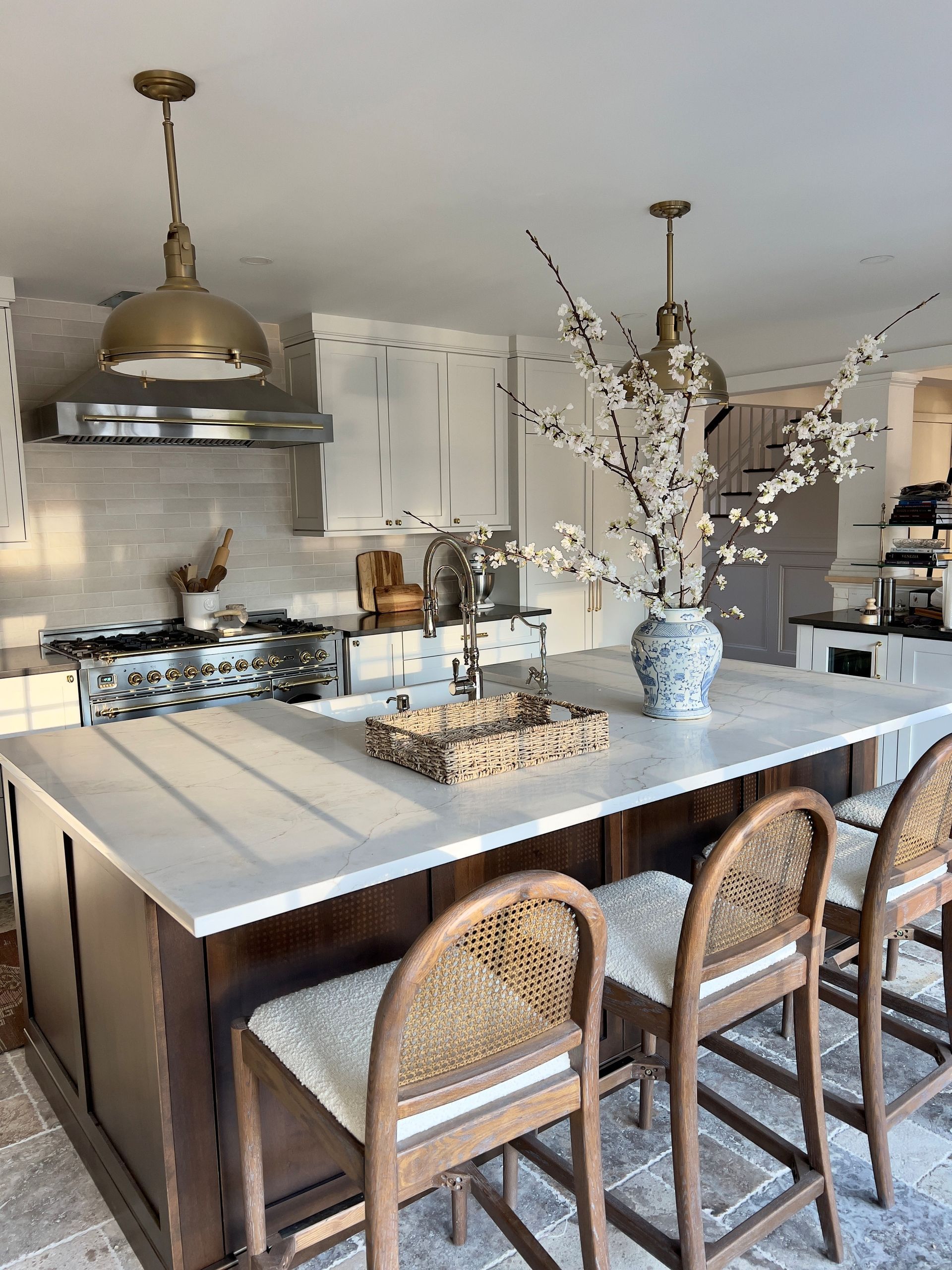 Modern kitchen with large island, wicker stools, brass pendant lights, and white floral centerpiece