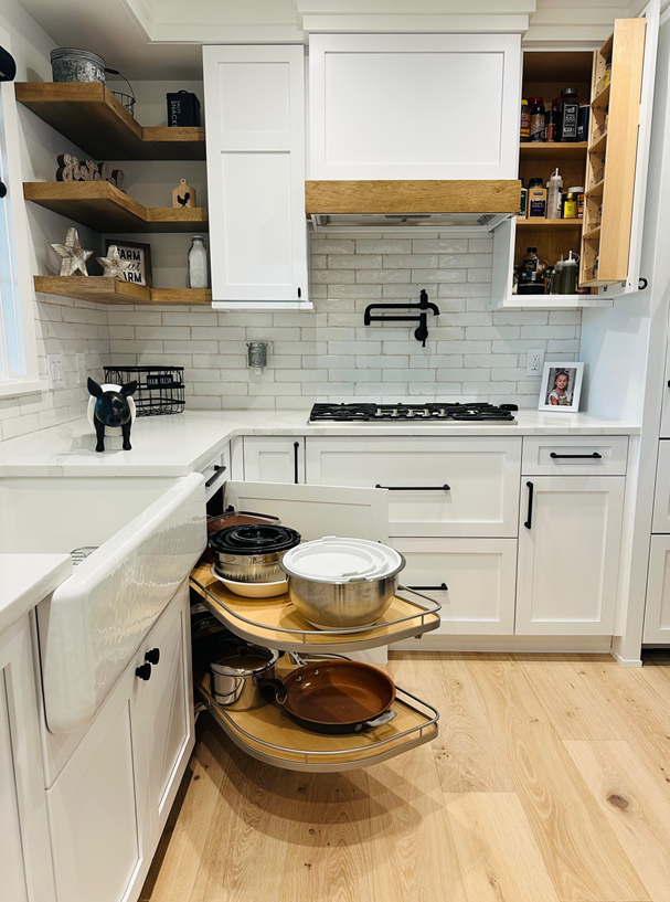 Bright white kitchen with wood shelves, gas stove, and a rolling cart of cookware in the center.