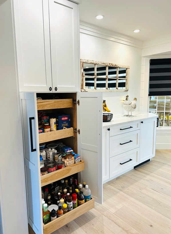 Bright white kitchen with pull-out pantry shelves and a sink under a window.