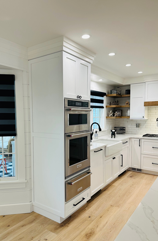 Bright white modern kitchen with built-in ovens, open shelves, and light wood floors.