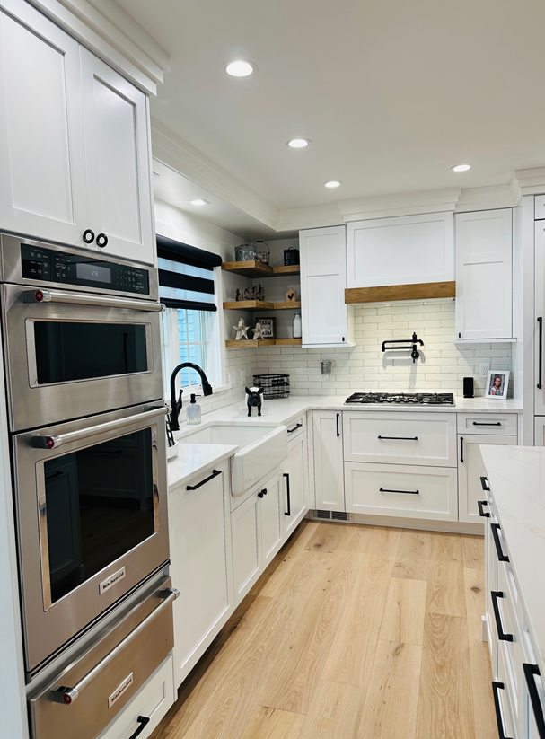 Bright white modern kitchen with stainless steel double ovens and light wood floor