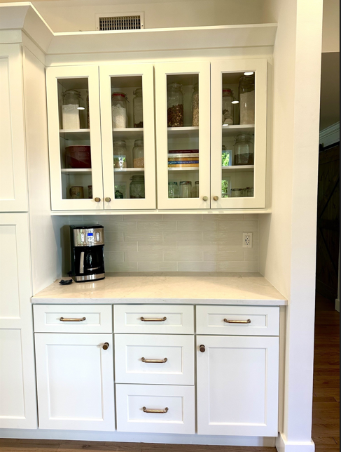 White built-in kitchen hutch with glass cabinets, drawers, and a black coffee maker on the counter.
