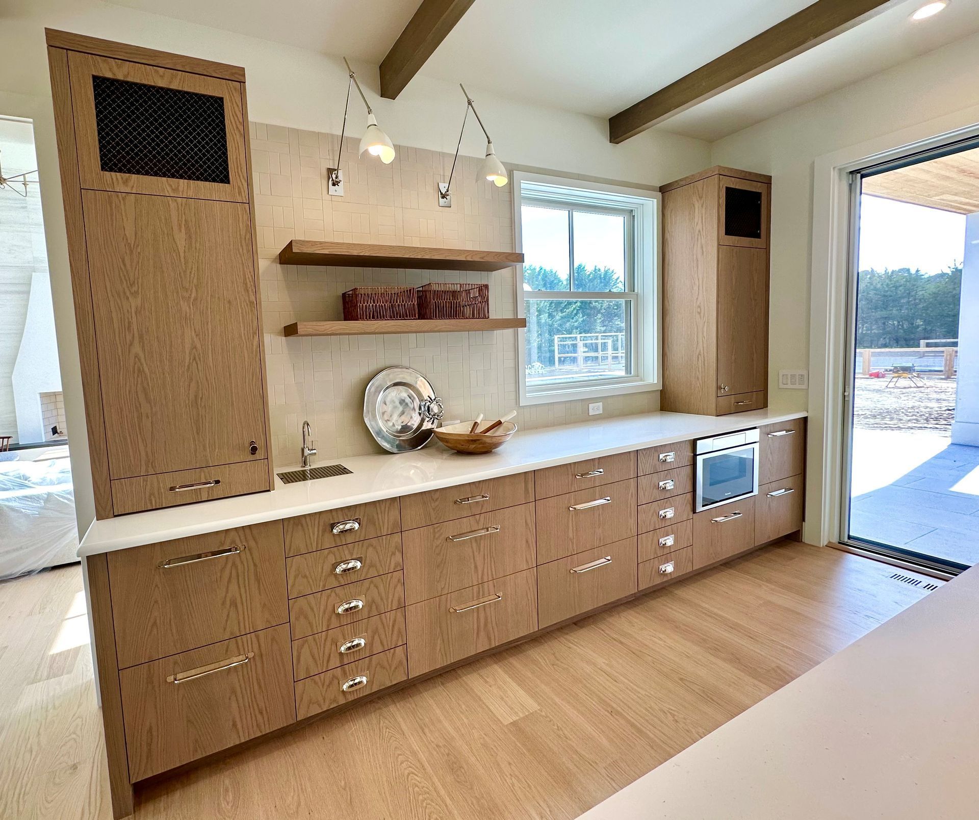 Bright kitchen with wood cabinets, white countertops, open shelves, and a large window overlooking outside