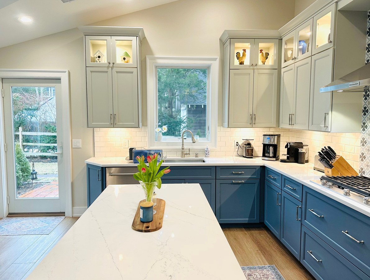 Bright modern kitchen with blue cabinets, white island, and large windows overlooking greenery