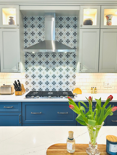 Blue-and-white kitchen with floral tile backsplash, stainless range hood, and tulips on the island
