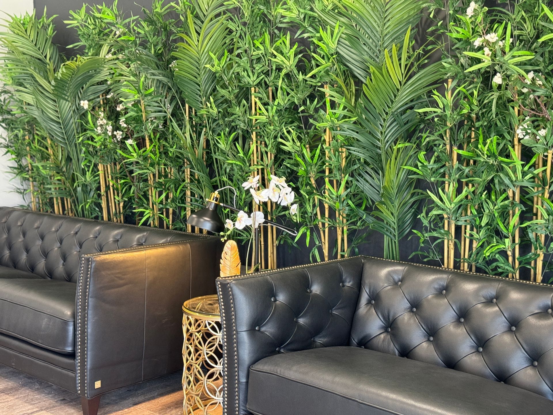 Black tufted leather sofas in a lounge with a wall of green plants and white flowers