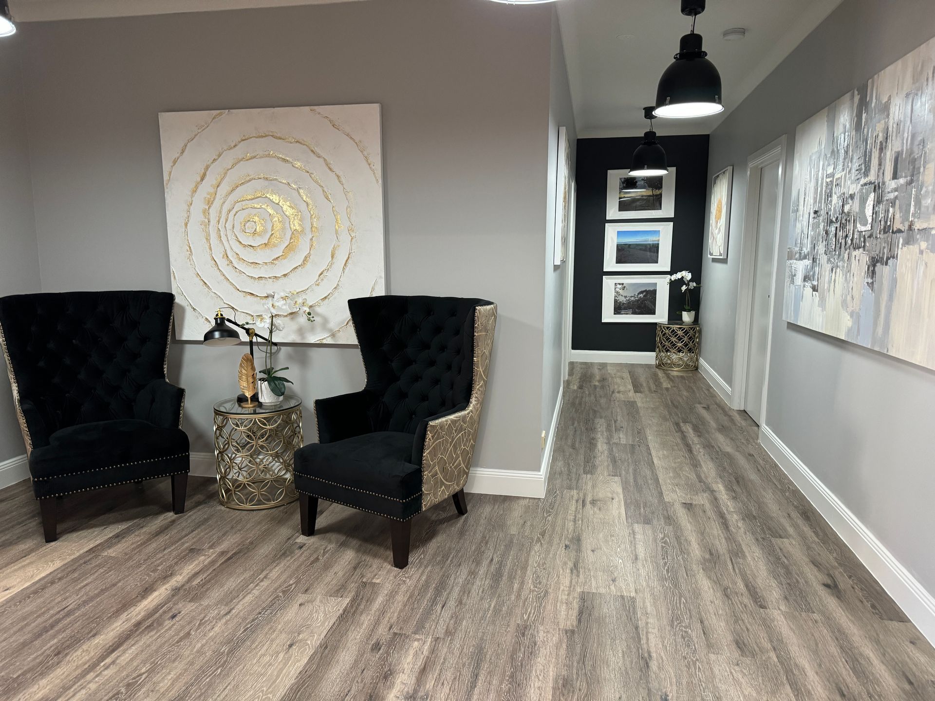 Modern office lounge with two black armchairs, a small table, and abstract wall art in a gray hallway.