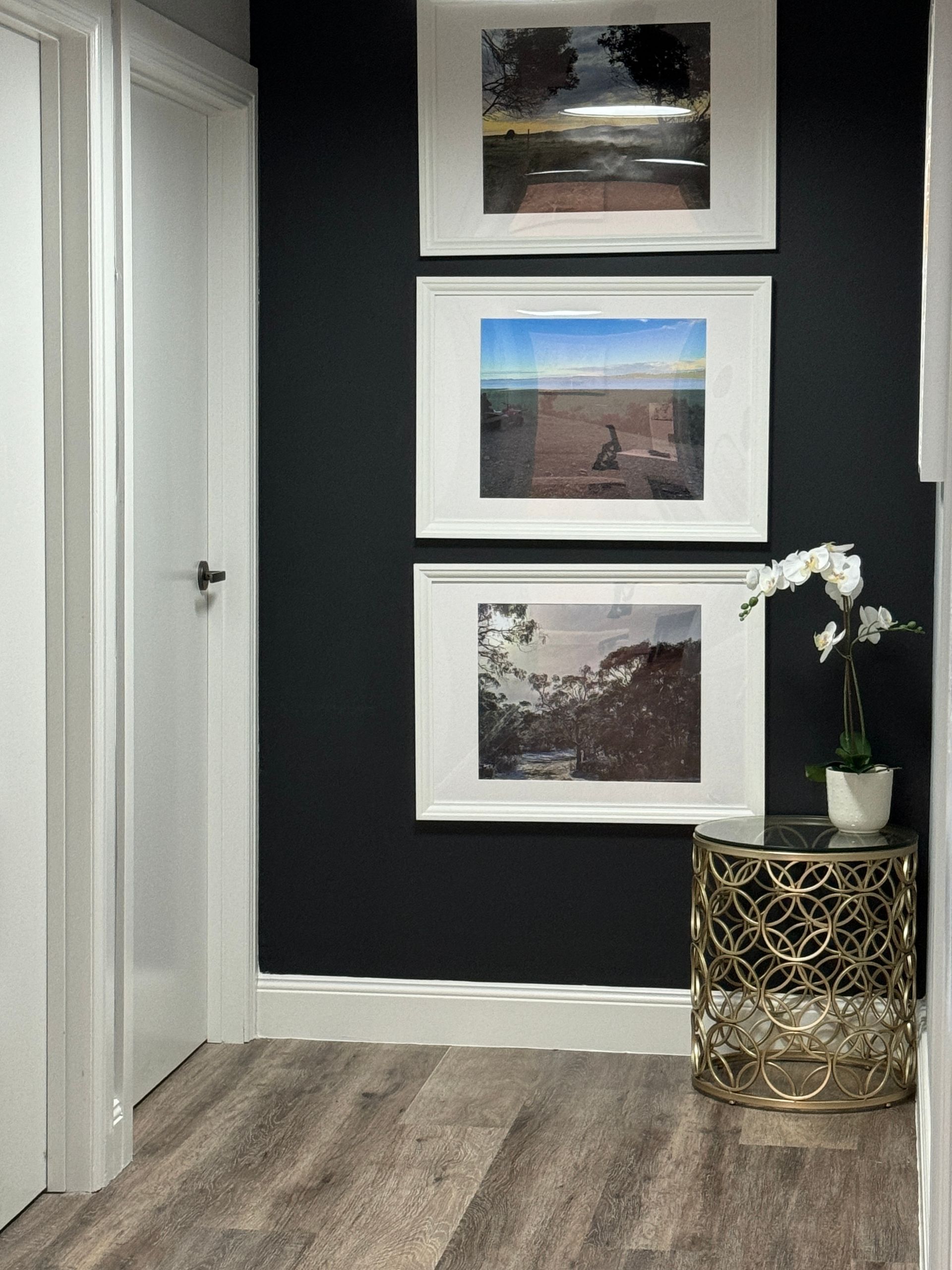 Hallway with dark accent wall, three framed landscape photos, white flowers, and gold side table