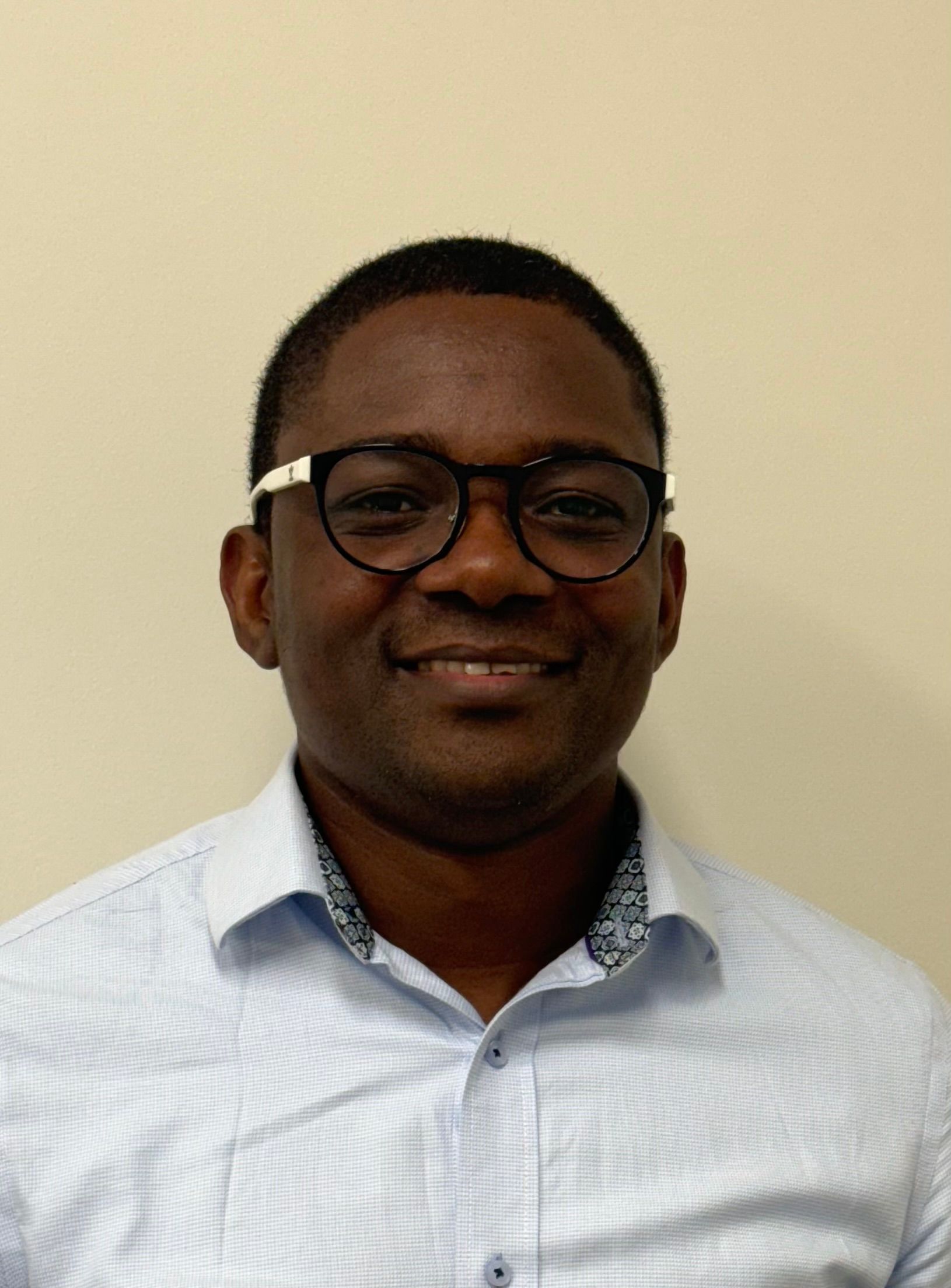 Smiling man in glasses and a light blue shirt against a beige background