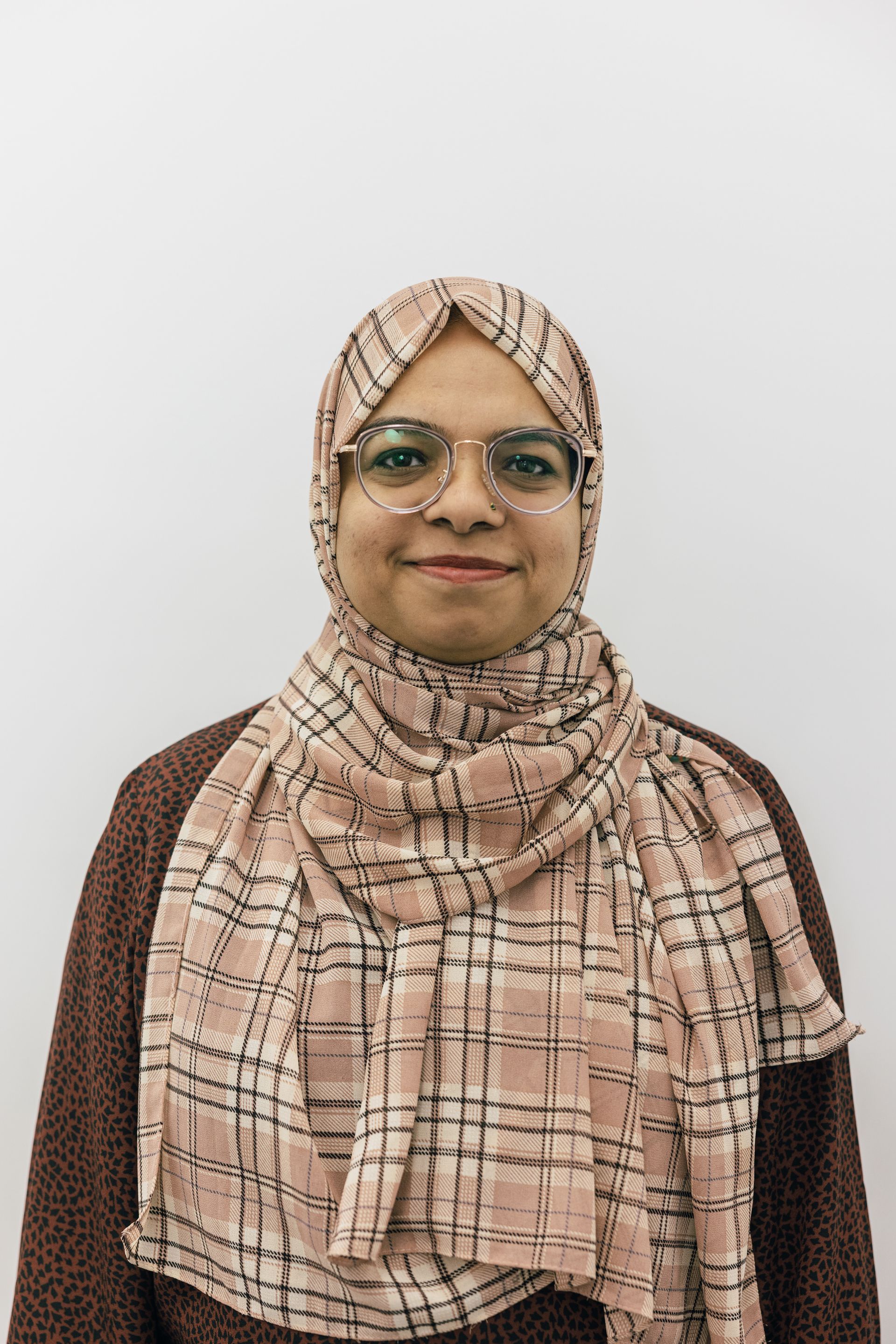 Portrait of a person wearing glasses and a beige plaid hijab against a plain light background