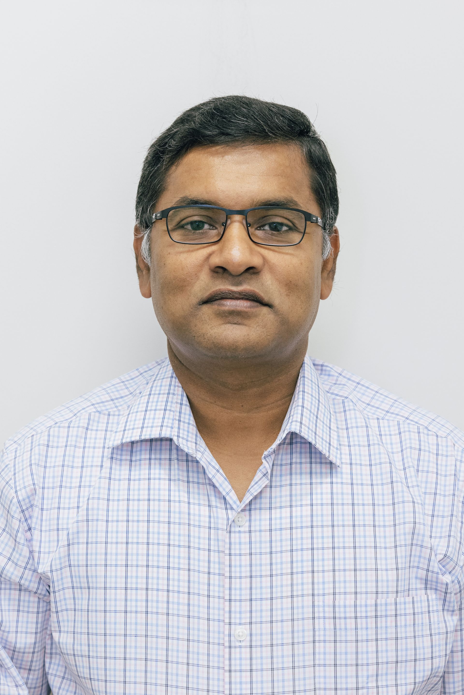 Portrait of a man wearing glasses and a light checkered shirt against a plain white background