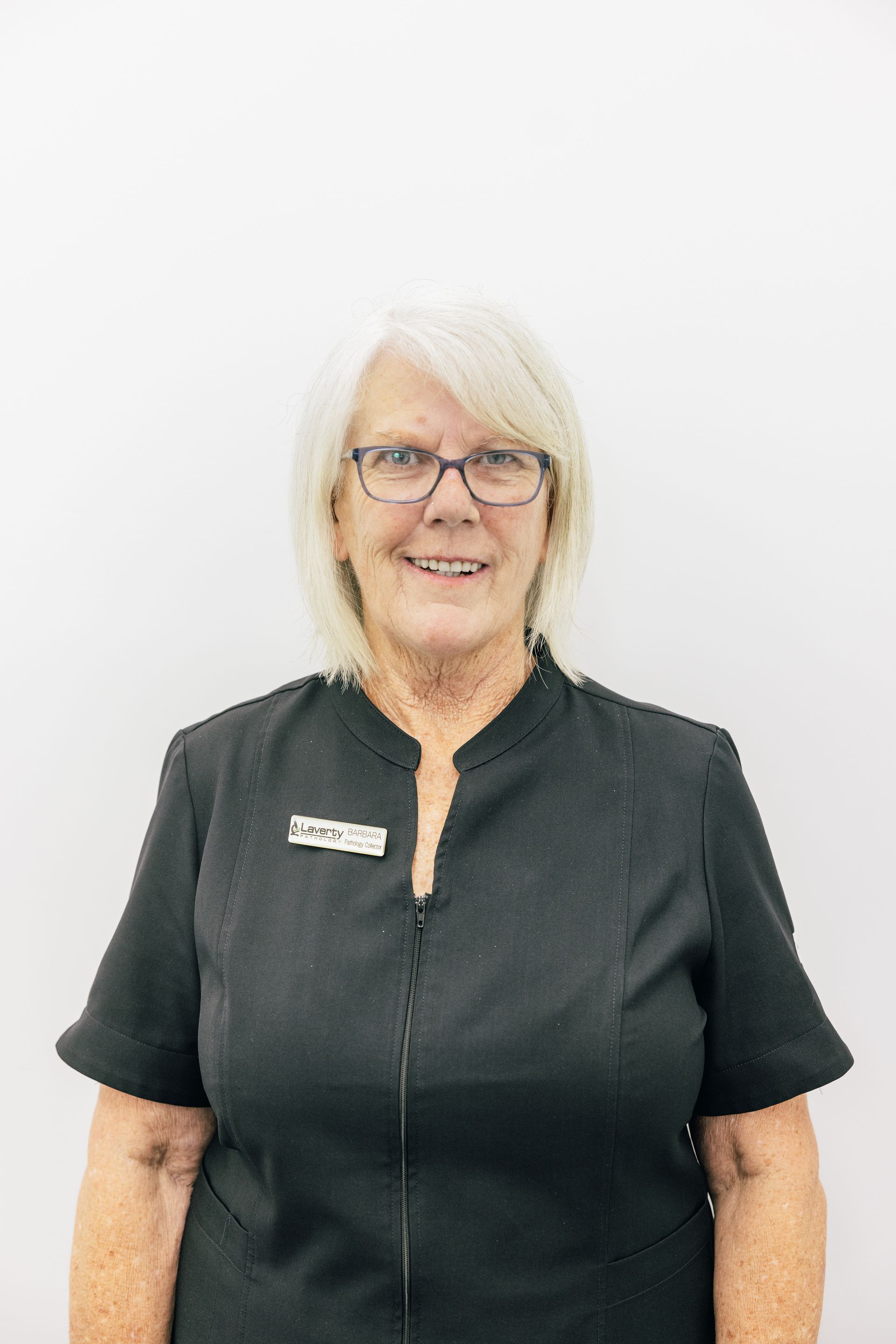 Portrait of a woman with blonde hair and glasses, wearing a black shirt and smiling against a white background