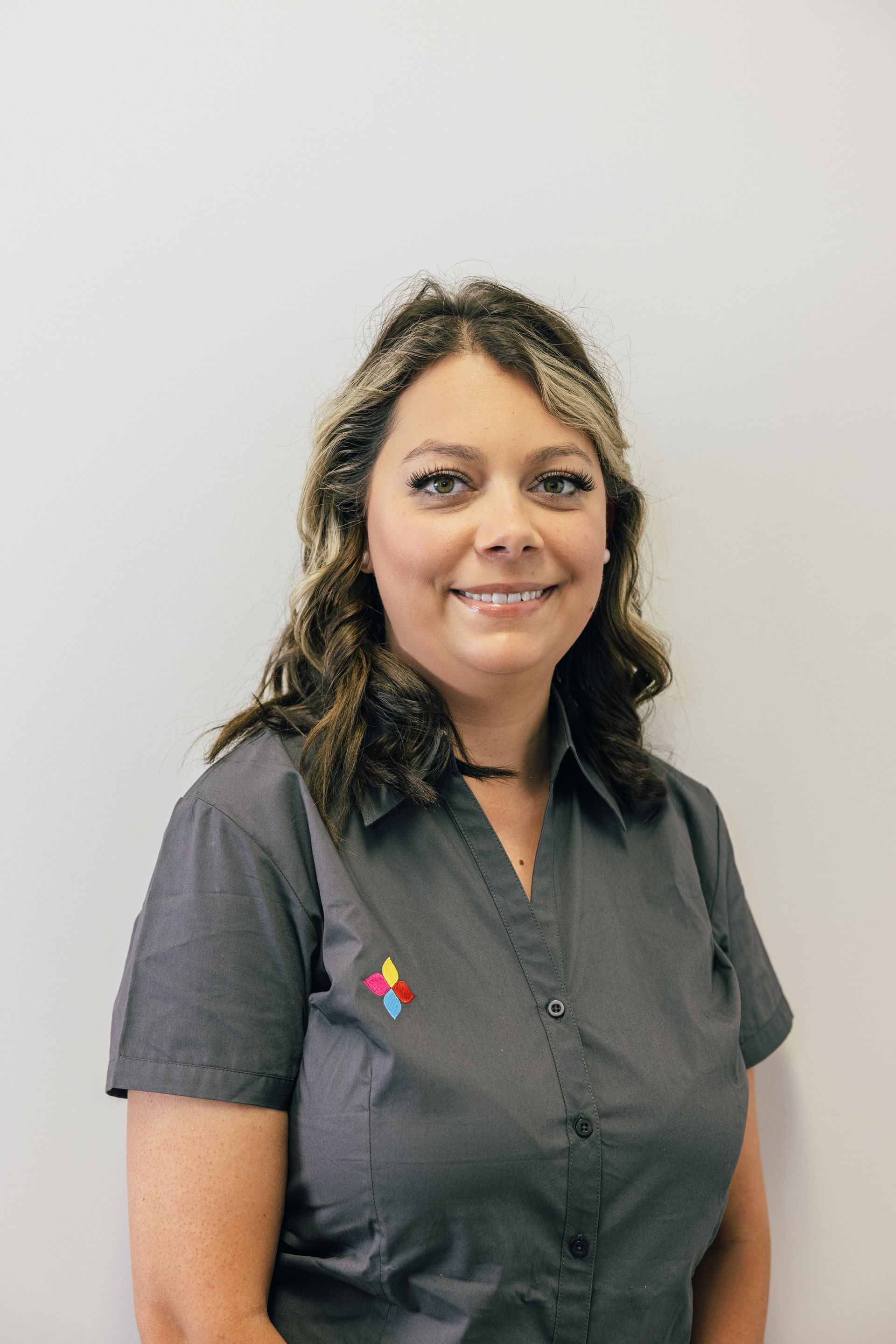 Woman in gray shirt smiling against a plain light wall.